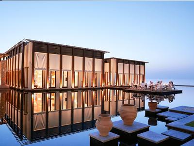 Modernes Gebäude mit großen Fenstern am Wasser, Spiegelung im ruhigen See, klare blaue Abendstimmung.