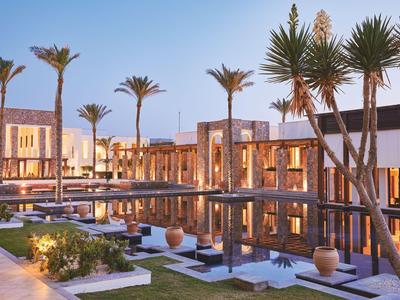 Complesso alberghiero moderno con sentieri illuminati, giochi d'acqua e palme al tramonto.