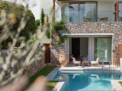 Moderner Außenbereich mit Pool und Sitzgelegenheiten vor einer steinverkleideten Ferienvilla.