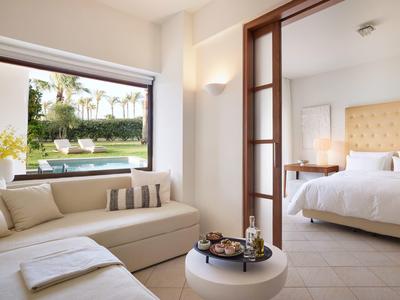 Modernes Hotelzimmer mit gemütlichem Sofa, großem Fenster und Blick auf Garten mit Pool.
