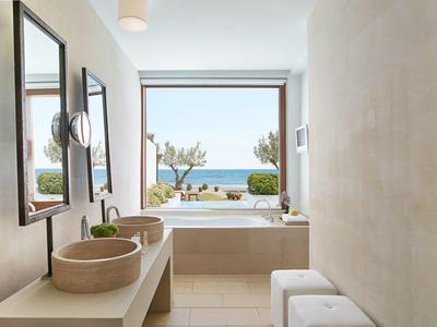 Modernes Badezimmer mit Fenster zum Meer, großer Badewanne, Doppelwaschbecken und zwei Hockern.
