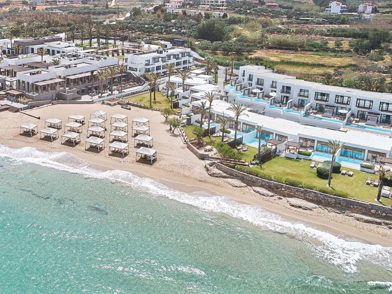 Strandresort mit weißen Liegestühlen, blauem Meer und Hotelgebäuden im Hinterland.