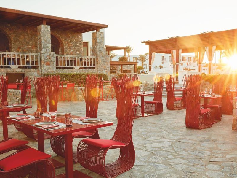 Außenbereich eines Restaurants mit roten Stühlen und Tischen bei Sonnenuntergang.