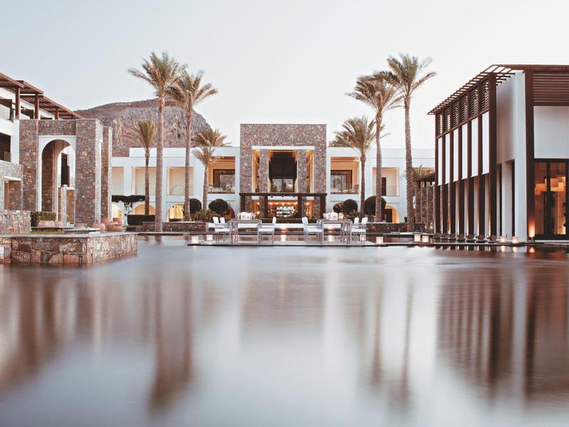 Luxuriöses Hotel mit Pool, Palmen und moderner Architektur in warmen, gedeckten Farben.