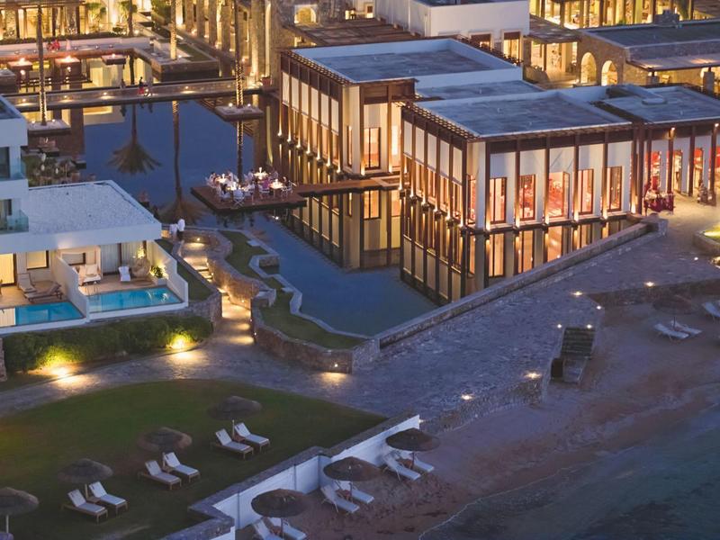 Beleuchtetes modernes Hotel mit Pool und Liegen am Strand in der Dämmerung.