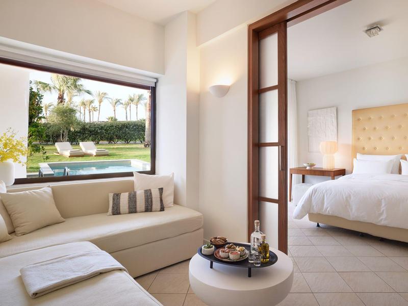 Modernes Hotelzimmer mit gemütlichem Sofa, großem Fenster und Blick auf Garten mit Pool.