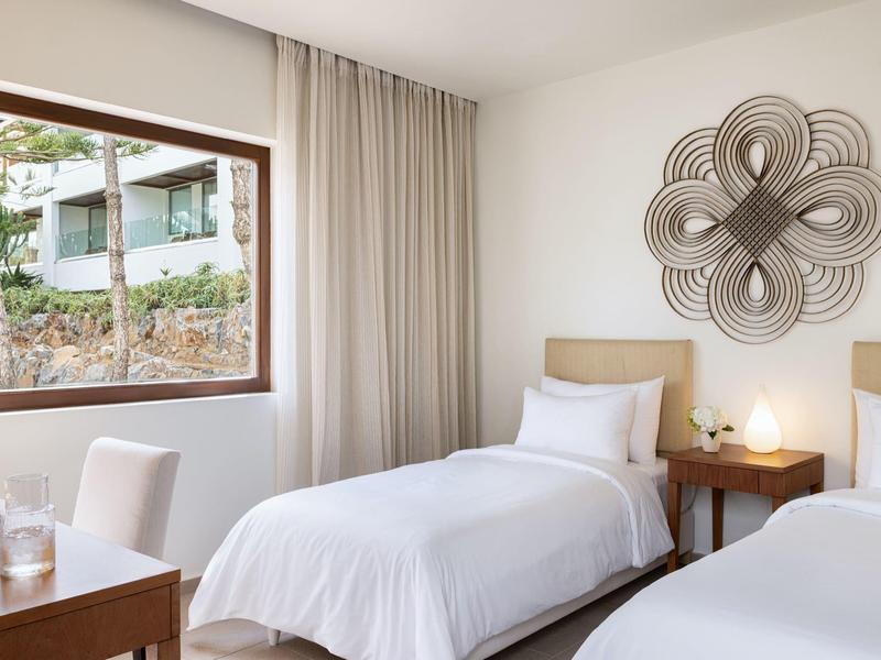 Helles Hotelzimmer mit zwei Einzelbetten, Nachttisch und großem Fenster mit Blick ins Grüne.