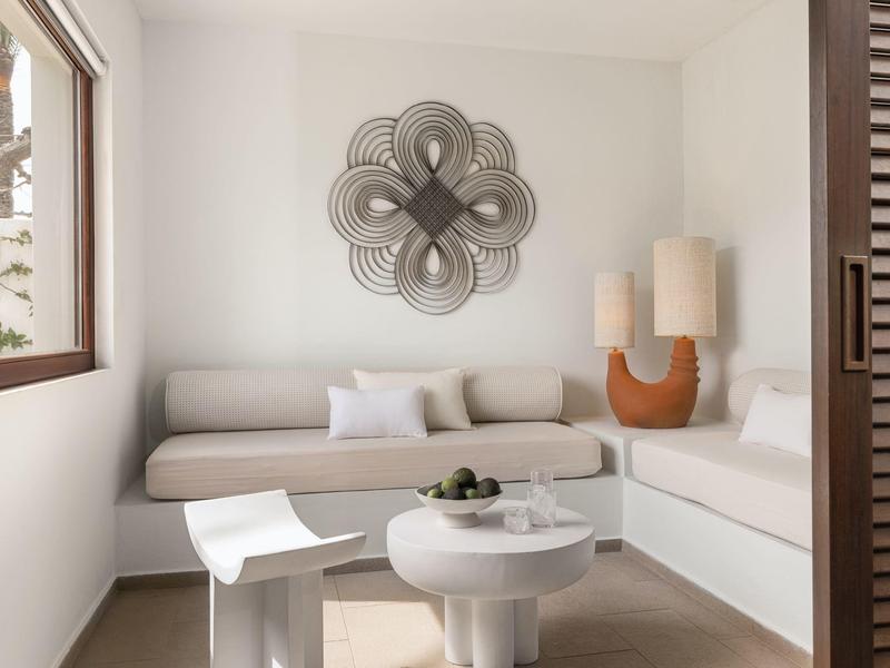 Helles Wohnzimmer mit modernen weißen Möbeln, dekorativer Wandkunst und großem Fenster.