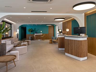 Moderní hotelová lobby s recepcí, posezením a dekorativními rostlinami.