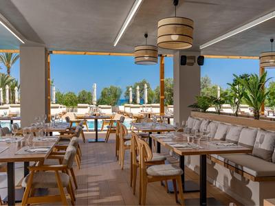 Moderní venkovní restaurace s dřevěnými židlemi a výhledem na bazén a palmy.