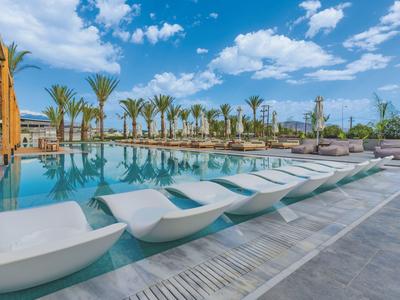 Area piscina moderna con lettini bianchi, palme e cielo blu in un resort.