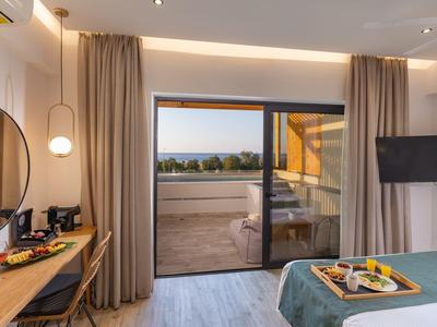 Moderní hotelový pokoj s balkonem, manželskou postelí, TV a psacím stolem s výhledem na krajinu.