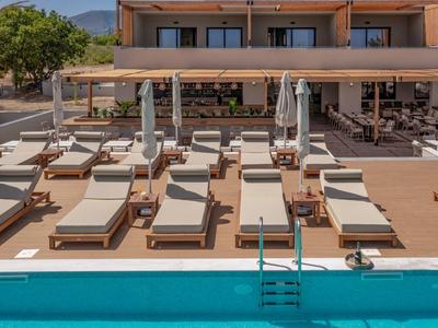 Několik bílých lehátek s deštníky vedle modrého bazénu na hotelové terase.