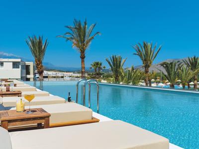 Langer Poolbereich mit weißen Liegen und Palmen vor klarem blauem Himmel.