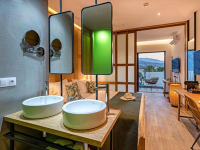 Modernes Hotelzimmer mit Doppelwaschbecken, Spiegeln und Blick auf Terrasse mit Meerblick.