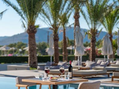 Moderní jídelní stůl se židlemi a nápoji u bazénu obklopeného palmami.