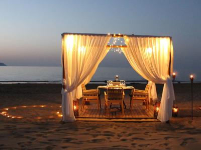 Romantická večeře pod osvětleným pavilonem na pláži při západu slunce.