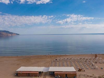 Prázdná písečná pláž s deštníky a dvěma malými budovami u klidného moře pod modrou oblohou.