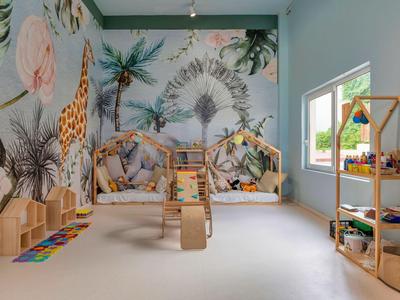 Barevný, přátelský dětský pokoj s nástěnnými malbami, hračkami a regály vedle velkého okna.