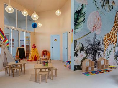 Dětský herní pokoj se stoly, židlemi, stanem, malbou žirafy a hrami ve tvaru domu.