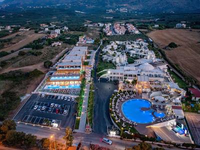 Letecký pohled na resort s kulatým bazénem, parkovišti a okolní krajinou za soumraku.