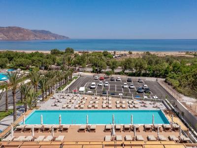 Pohled na bazén s lehátky, palmami a mořem v pozadí za jasného počasí.