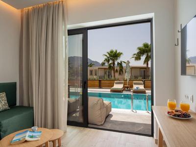 Moderní hotelový pokoj s terasou s výhledem na bazén a palmy.