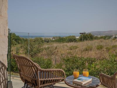 Dva proutěné křesla a stůl na terase s výhledem na pole a moře.