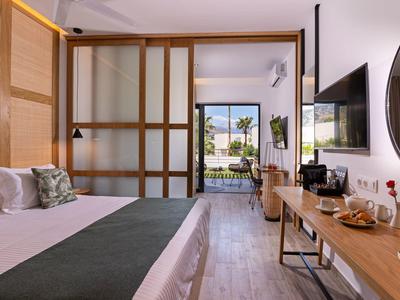 Světle zařízený hotelový pokoj s výhledem na terasu a zahradu přes velká okna.