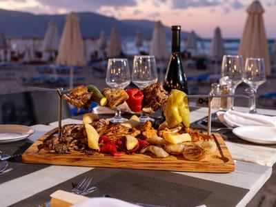 Elegantně naaranžovaná večeře na dřevěné desce s vínem a plážovým pozadím při západu slunce.