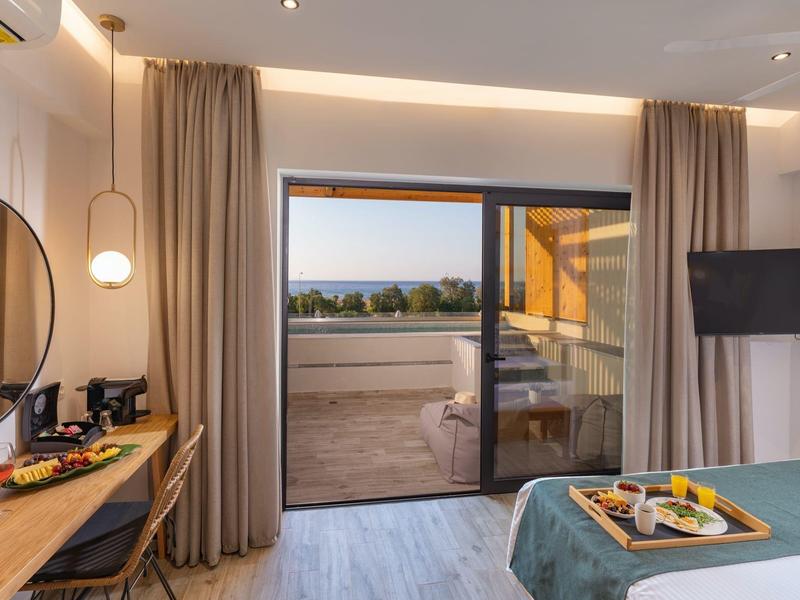 Moderní hotelový pokoj s balkonem, manželskou postelí, TV a psacím stolem s výhledem na krajinu.