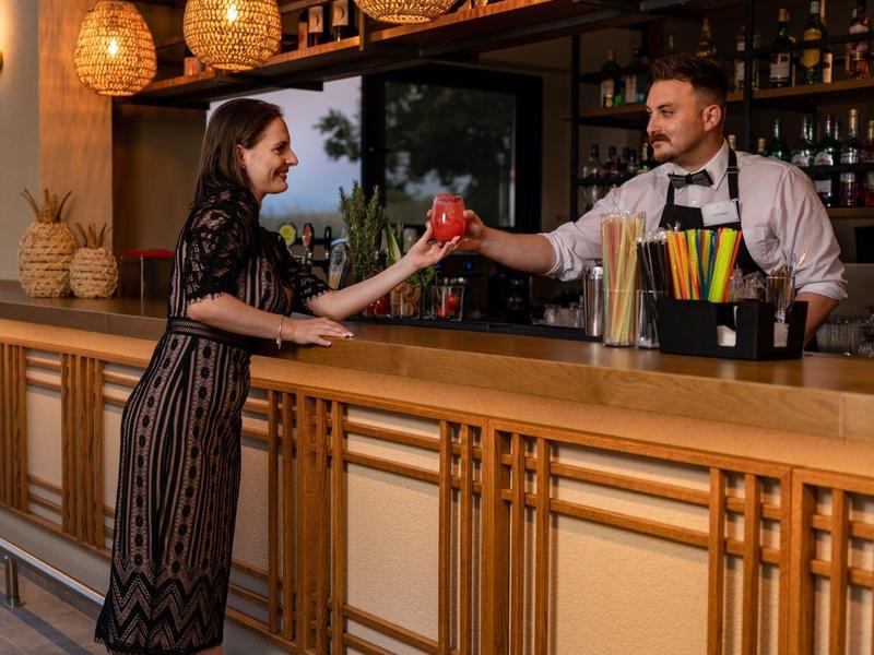 Elegantní žena objednává koktejl u stylového hotelového baru s teplým osvětlením.