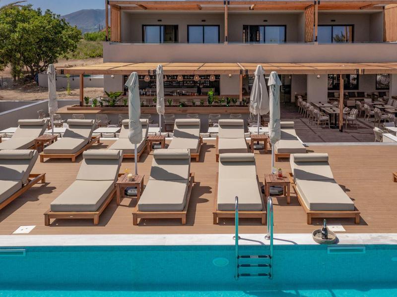 Několik bílých lehátek s deštníky vedle modrého bazénu na hotelové terase.