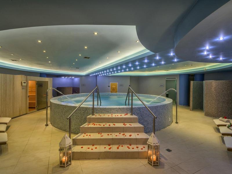 Interiér wellness oblasti s kulatou vířivkou, měkkým osvětlením a lehátky.