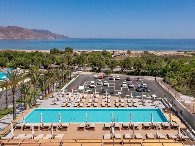 Pohled na bazén s lehátky, palmami a mořem v pozadí za jasného počasí.