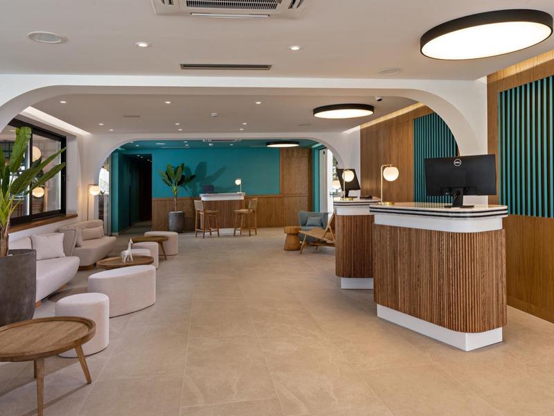 Moderní hotelové lobby s posezením, rostlinami a recepcí v teplých tónech.