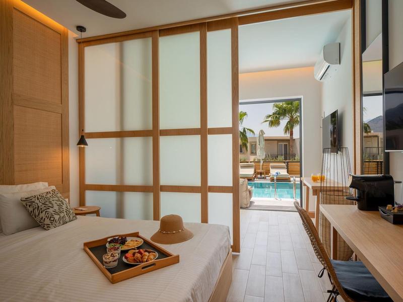 Moderní hotelový pokoj s výhledem na bazén a terasu, světlý dřevěný design a útulná postel.