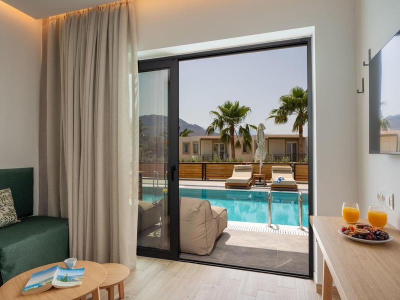 Moderní hotelový pokoj s terasou s výhledem na bazén a palmy.