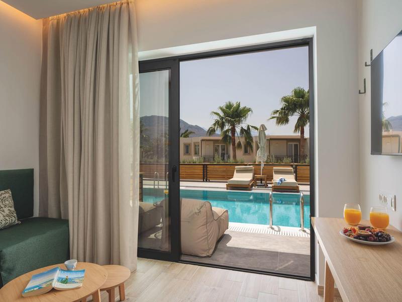 Moderní hotelový pokoj s výhledem na bazén a palmy přes velké posuvné dveře