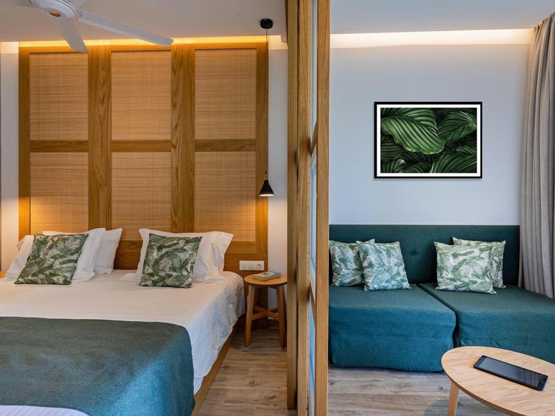 Moderně zařízený hotelový pokoj s manželskou postelí, pohovkou a dřevěným obložením.