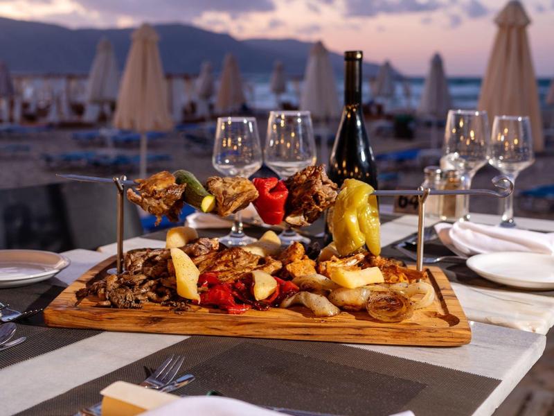 Elegantně naaranžovaná večeře na dřevěné desce s vínem a plážovým pozadím při západu slunce.