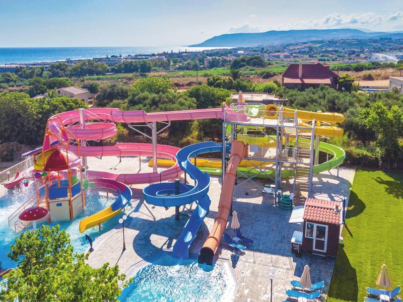 Barevný vodní park s tobogány, bazény a slunečními plochami v slunné krajině.