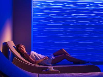 Kobieta relaksująca się na leżaku przy teksturowanej ścianie o niebieskim świetle, atmosfera spa.