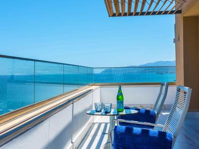 Balcon avec deux chaises, serviette bleue et vue sur la mer sous un ciel clair.