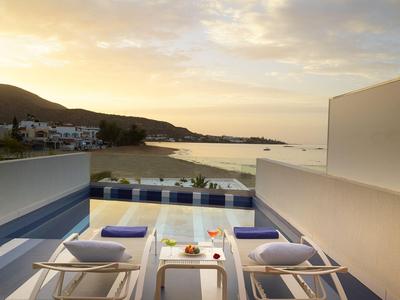 Vue sur une piscine avec des chaises longues et une côte méditerranéenne au coucher du soleil.