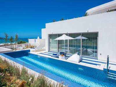 Piscine blanche moderne avec chaises longues et parasols à côté d'une maison avec vue sur la mer.