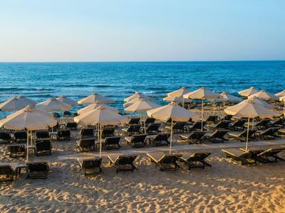Plaża z rzędami leżaków i parasoli nad morzem o zachodzie słońca.