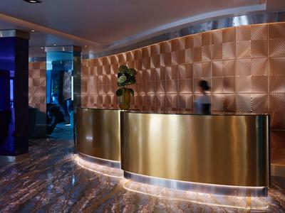 Nowoczesna recepcja hotelowa z złotym barem i teksturowaną ścianą, stylowy klimat i przytłumione oświetlenie.