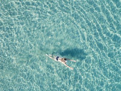Osoba pływa w przezroczystej, turkusowej wodzie widziana z góry.