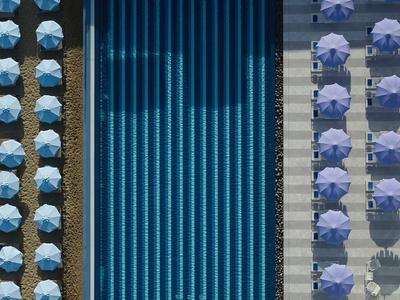 Długi niebieski basen z parasolami ułożonymi po obu stronach, widok z lotu ptaka hotelu.